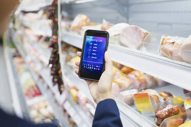 Frau mit digitaler Einkaufsliste auf Fotohandy im Supermarkt - CAIF27295