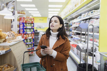Frau mit Smartphone beim Einkaufen im Supermarkt - CAIF27296