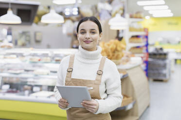 Portrait confident female grocer with digital tablet working in supermarket - CAIF27310