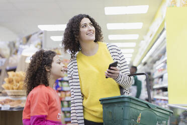 Mutter und Tochter mit Smartphone beim Einkaufen im Supermarkt - CAIF27316
