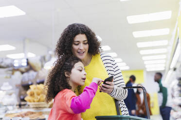 Mutter und Tochter mit Smartphone beim Einkaufen im Supermarkt - CAIF27318