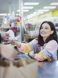 Lächelnde, freundliche Kassiererin, die einem Kunden an der Supermarktkasse eine Quittung gibt - CAIF27322
