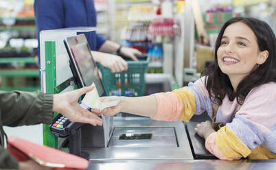 Lächelnde Kassiererin gibt dem Kunden an der Supermarktkasse eine Quittung - CAIF27325