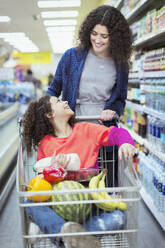 Glückliche Mutter, die ihre Tochter im Einkaufswagen im Supermarkt schiebt - CAIF27327