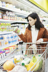 Frau liest Etikett auf Behälter im Supermarkt - CAIF27328