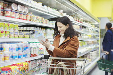 Lächelnde Frau liest das Etikett auf einem Behälter im Supermarkt - CAIF27331