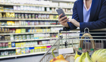 Frau mit Smartphone beim Einkaufen im Supermarkt - CAIF27332