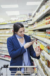 Frau mit Smartphone scannt Etikett auf Glas im Supermarkt - CAIF27337