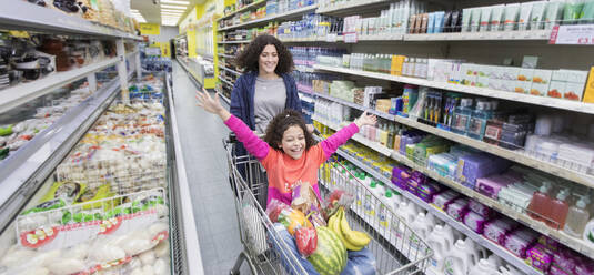 Mutter schiebt verspielte Tochter im Einkaufswagen im Supermarktgang - CAIF27339