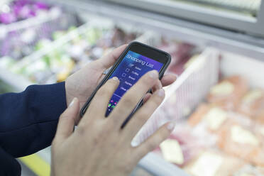 Close up woman using smart phone shopping list app in supermarket - CAIF27352