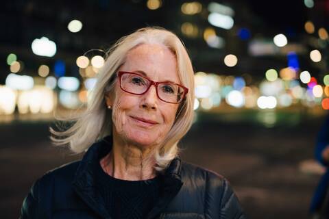 Portrait of wrinkled smiling woman standing in illuminated city at night stock photo