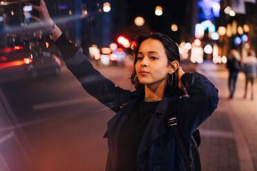 Young woman with hand in hair hailing for taxi in city at night - MASF17952