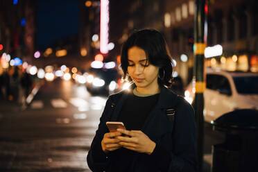 Junge Frau benutzt ein Mobiltelefon, während sie nachts in der Stadt steht - MASF17967