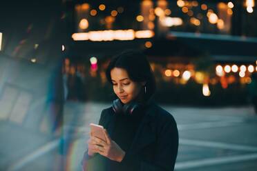 Junge Frau benutzt ein Mobiltelefon, während sie nachts in der Stadt steht - MASF17985