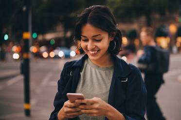 Lächelnde junge Frau, die soziale Medien auf ihrem Handy nutzt, während sie in der Stadt steht - MASF18011