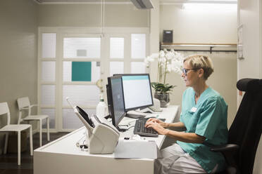 Seitenansicht einer reifen Ärztin, die am Computer arbeitet, während sie in einer Klinik sitzt - MASF18038