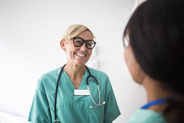 Lächelnder reifer Kinderarzt im Gespräch mit einer Mitarbeiterin, während er in der Klinik steht - MASF18043