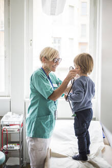 Lächelnde Ärztin hält Stethoskop an das Ohr eines Jungen im Krankenhaus - MASF18053