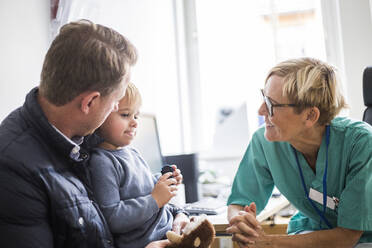 Lächelnder reifer Arzt im Gespräch mit einem Jungen mit Vater in der Klinik - MASF18054