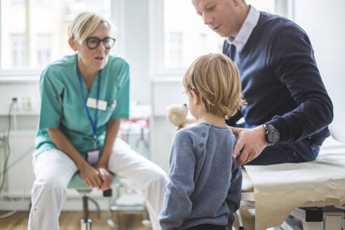 Rückansicht eines Jungen, der neben seinem Vater steht und mit einem Arzt in der Klinik spricht - MASF18057