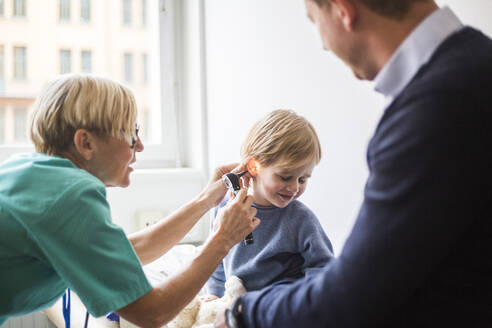 Ärztin, die das Ohr eines Jungen mit einem Otoskop untersucht, während ihr Vater im Krankenhaus sitzt - MASF18058