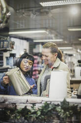 Saleswoman showing kettle to smiling female customer in store seen through glass window - MASF18075