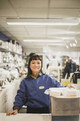 Portrait of smiling saleswoman with appliance standing in electronics store - MASF18079