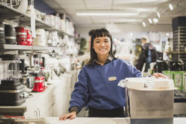 Portrait of smiling saleswoman with appliance standing in store - MASF18080