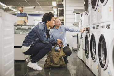 Älterer Besitzer erklärt einem Kunden in einem Elektronikgeschäft die Waschmaschine - MASF18118