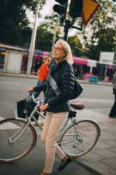 Ältere Frau mit Fahrrad beim Überqueren der Straße in der Stadt - MASF18160