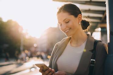 Smiling woman messaging while standing in city - MASF18181