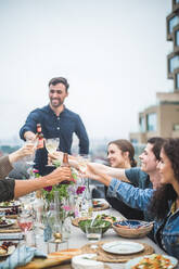 Young man toasting drinks with friends during social gathering on rooftop - MASF18228