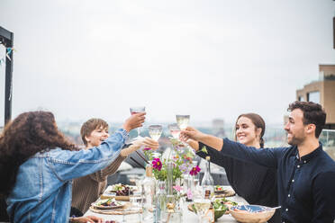 Männliche und weibliche Freunde stoßen mit Wein an, während sie zum Abendessen auf der Terrasse sitzen - MASF18237