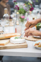 Abgeschnittene Hände eines Mannes, der Mozzarella auf einem Schneidebrett auf der Terrasse eines Gebäudes während einer Party schneidet - MASF18242