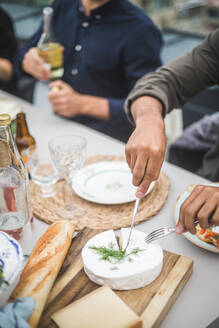 Hohe Winkel Ansicht des Mannes Schneiden Mozzarella über Schneidebrett am Gebäude Terrasse während der Party - MASF18243