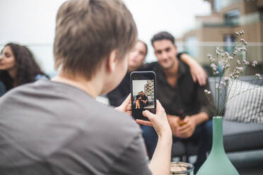 Rückansicht einer Frau, die während einer Terrassenparty Freunde mit ihrem Smartphone fotografiert - MASF18253