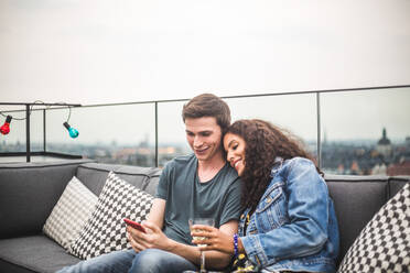 Lächelnder Mann, der seiner Partnerin auf der Terrasse bei einem Getränk sein Smartphone zeigt - MASF18255