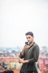 Man using smart phone while standing on terrace against sky - MASF18262