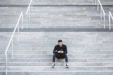 Junger Mann benutzt sein Smartphone, während er auf einer Treppe sitzt - MASF18357