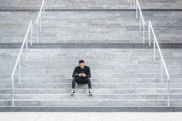 Young man using mobile phone while sitting on staircase - MASF18358
