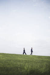 Side view of friends walking on grassy field against cloudy sky - MASF18376