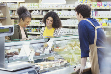 Arbeiter hilft Frauen an der Bäckereivitrine im Supermarkt - CAIF27357