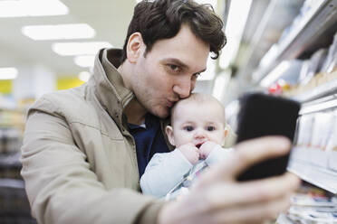 Affectionate father and baby daughter taking selfie in supermarket - CAIF27362