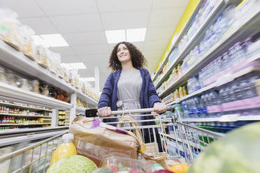 Woman pushing shopping cart in supermarket aisle - CAIF27363