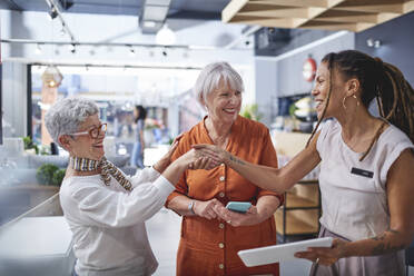 Innenarchitektin beim Händeschütteln mit Frauen, die in einem Geschäft für Wohnkultur einkaufen - CAIF27397