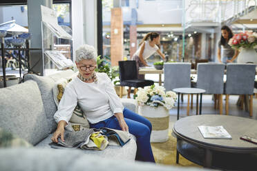 Ältere Frau betrachtet Stoffmuster auf einem Sofa in einem Einrichtungsgeschäft - CAIF27403