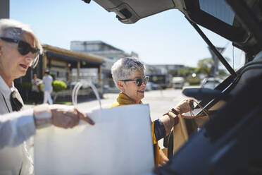 Senior women loading shopping bags into back of car in sunny parking lot - CAIF27406