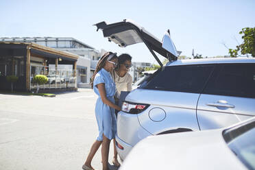 Frauen laden auf einem sonnigen Parkplatz Einkaufstüten in den Kofferraum eines Autos - CAIF27419