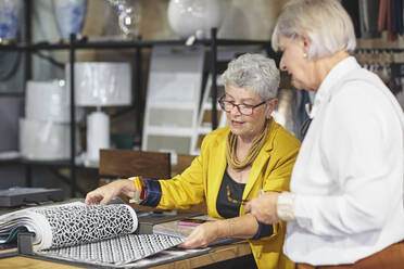 Senior women looking at fabric swatches in home decor shop - CAIF27424