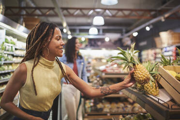 Frau beim Einkaufen von Ananas in der Gemüseabteilung eines Supermarkts - CAIF27437